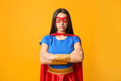 Confident young woman wearing superhero costume on orange background