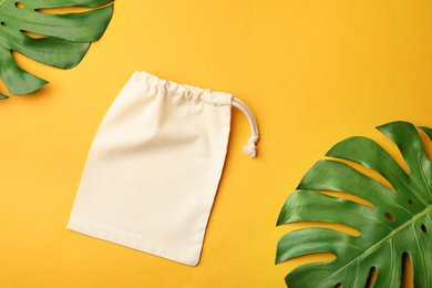Cotton eco bag and leaves on yellow background, flat lay