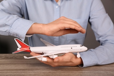 Insurance agent covering toy plane at table, closeup. Travel safety concept