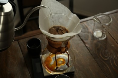 Photo of Barista pouring hot water into coffee maker at wooden table in cafe, closeup