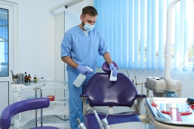 Professional dentist in uniform cleaning workplace  with antiseptic indoors