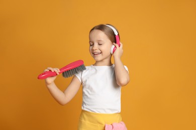 Photo of Cute little girl in headphones with brush singing on orange background
