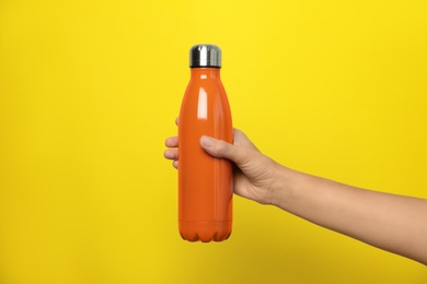 Woman holding modern orange thermos on yellow background, closeup