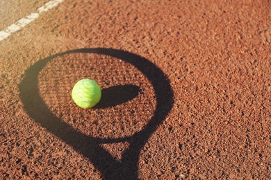 Shadow of racket and tennis ball on clay court. Space for text