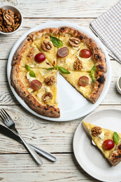 Photo of Delicious cheese pizza with walnuts and grapes served on white wooden table, flat lay