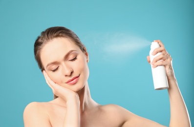 Young woman applying thermal water on face against color background. Cosmetic product