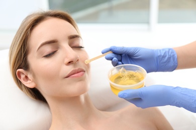 Beautiful woman getting wax epilation of face in salon