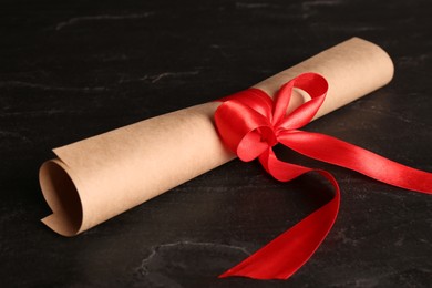 Photo of Rolled student's diploma with red ribbon on black table