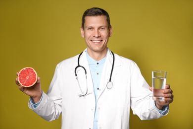 Nutritionist holding glass of pure water and ripe grapefruit on yellow background