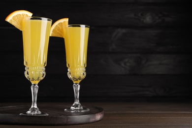 Glasses of Mimosa cocktail with garnish on wooden table. Space for text