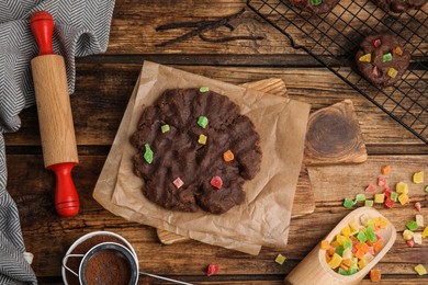 Unbaked chocolate cookies with candied fruits on wooden table, flat lay