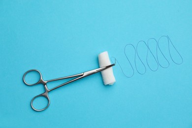 Forceps with suture thread and bandage roll on light blue background, flat lay. Medical equipment
