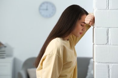 Stressed young woman near white brick wall at home