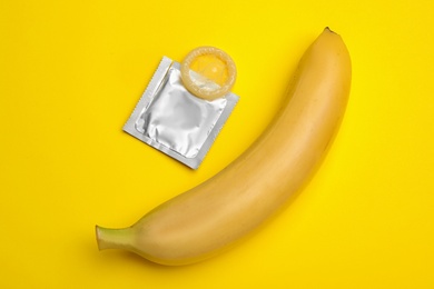 Condom and banana on yellow background, flat lay. Safe sex