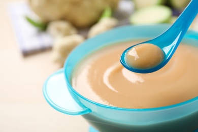 Spoon of healthy baby food over bowl on table, closeup