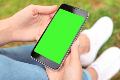 Image of Woman holding smartphone with green screen outdoors, closeup. Gadget display with chroma key. Mockup for design
