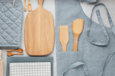 Kitchen napkins, apron and different utensils on light grey table, flat lay