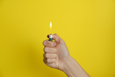Woman holding green lighter on yellow background, closeup