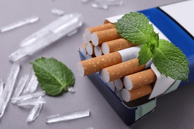 Pack of cigarettes, menthol crystals and mint leaves on grey background, closeup