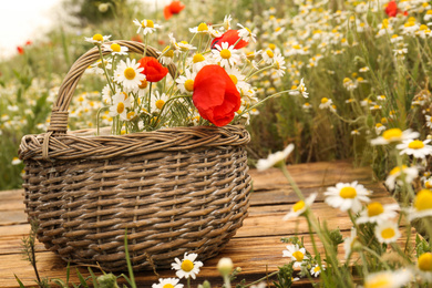Bouquet of poppies and chamomiles in wicker basket on wooden table outdoors