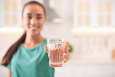 Young woman holding glass of pure water in kitchen, focus on hand