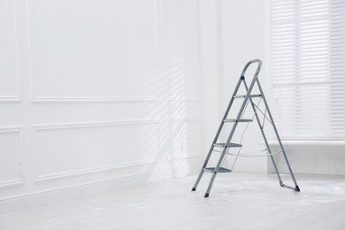Metal stepladder on floor covered with plastic in empty room, space for text