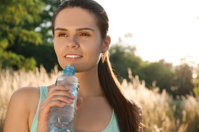 Happy young woman drinking water outdoors on hot summer day. Refreshing drink