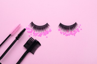 Flat lay composition with false eyelashes, confetti, makeup and mascara brushes on pink background