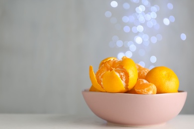 Tangerines in bowl on table against blurred lights, space for text