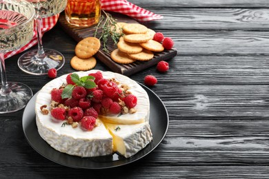 Brie cheese served with raspberries and walnuts on black wooden table. Space for text