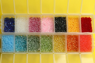Photo of Organizers with variety of colorful beads on yellow background, flat lay