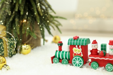 Bright toy train on artificial snow near small Christmas tree