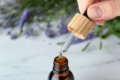 Photo of Woman pouring essential oil from pipette into bottle, closeup. Space for text