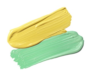 Strokes of green and yellow color correcting concealers on white background, top view