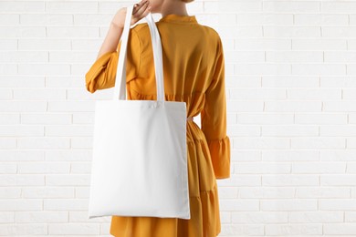 Woman with white textile bag near brick wall, closeup. Space for design