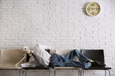 Human skeleton in office wear lying on chairs near brick wall indoors