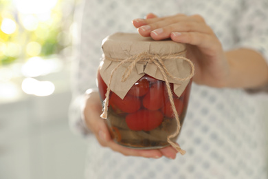 Woman holding jar of pickled tomatoes indoors, closeup