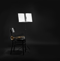 Trumpet, chair and note stand with music sheets on black background. Space for text