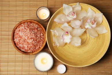 Photo of Bowl with water, flowers, sea salt and burning candles on bamboo mat, flat lay. Spa treatment