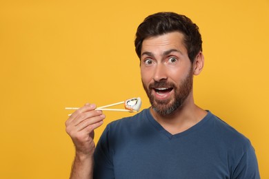 Photo of Happy man eating sushi roll with chopsticks on orange background