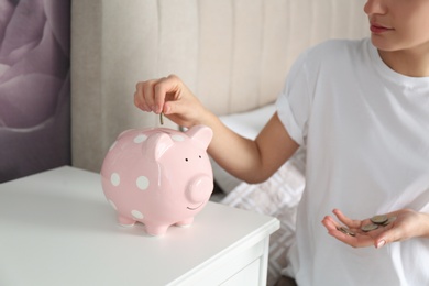 Woman putting money into piggy bank at nightstand indoors, closeup