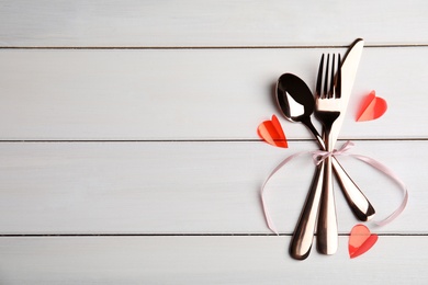 Cutlery set and pink ribbon on white table, top view with space for text. Valentine's day romantic dinner