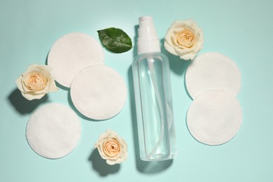 Bottle of micellar cleansing water, cotton pads and flowers on turquoise background, flat lay