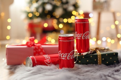 MYKOLAIV, UKRAINE - January 01, 2021: Cans of Coca-Cola and gifts on faux fur against blurred Christmas lights