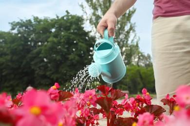 Photo of Man irrigating blooming plant with light blue watering can outdoors, closeup