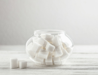 Refined sugar cubes in glass bowl on white wooden table