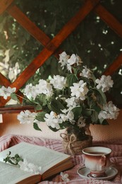 Bouquet of beautiful jasmine flowers in vase, open book and aromatic tea on fabric indoors