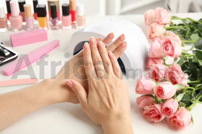 Woman doing manicure with ultraviolet nail lamp at white table, closeup