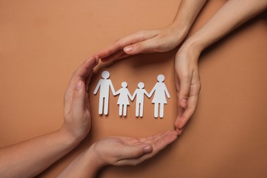 Couple protecting paper family figures on brown background, top view. Insurance concept