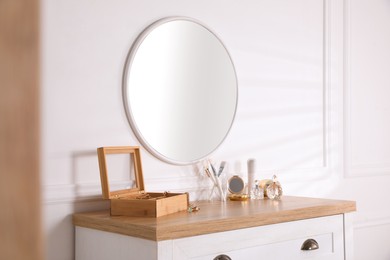 Photo of Trendy round mirror and chest of drawers with accessories near white wall indoors.